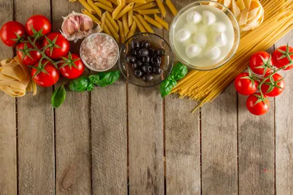 Tomaten, Pasta, Oliven, Knoblauch und Mozzarella auf einem Holztisch